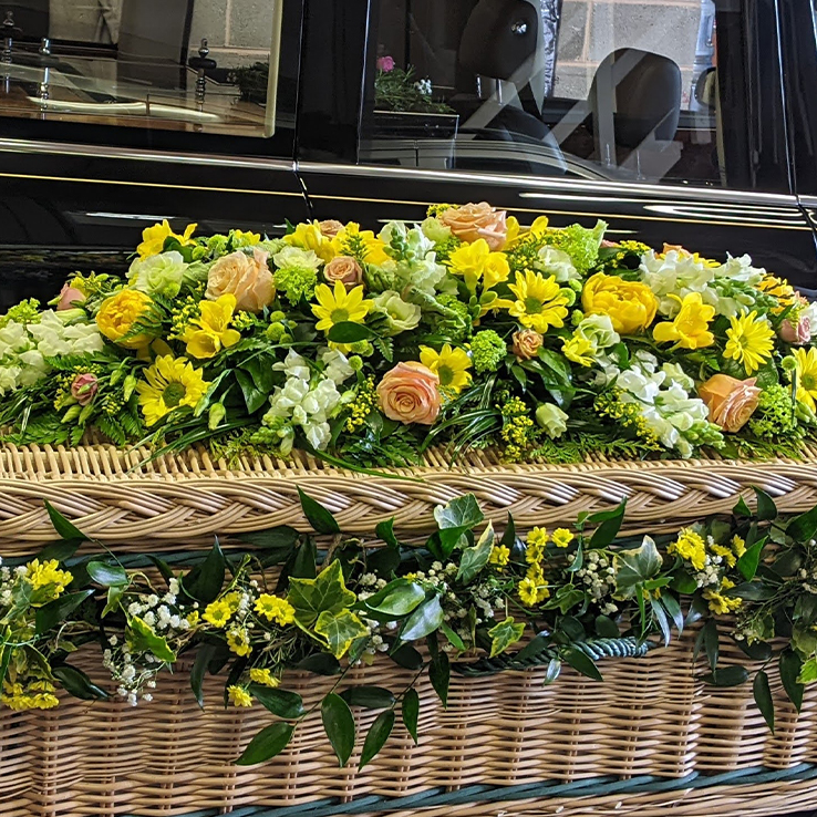 Market Harborough Funeral Flowers, Wicker casket with garlands of yellow daisies, gyposphilla & select greenery. Coordinating casket spray