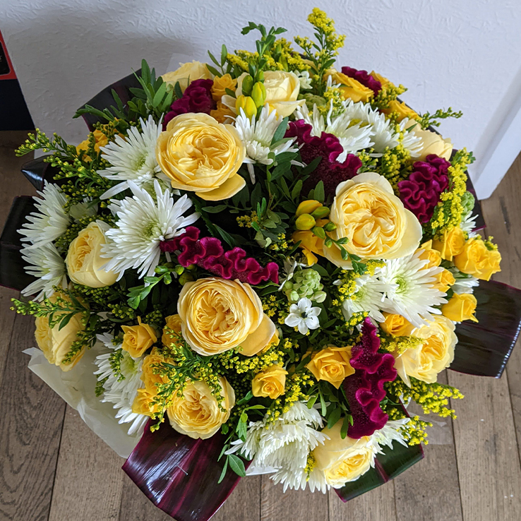 A luxury hand tied condolence bouquet with yellow multi petalled roses, white & burgandy flowers.