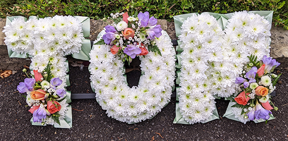 Oadby Funeral flowers, Wigston Funeral Flowers, Market Harborough Funeral Flowers, Leicester Funeral Flowers, Name tribute, traditional style with orange, white & lilac spray & green ribbon eadge